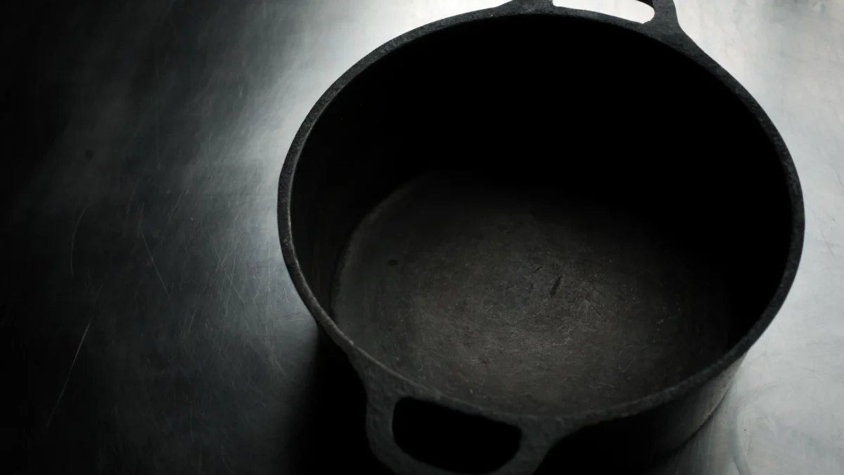 Panela de ferro fundido vazia sobre uma superfície de aço inoxidável iluminada suavemente.