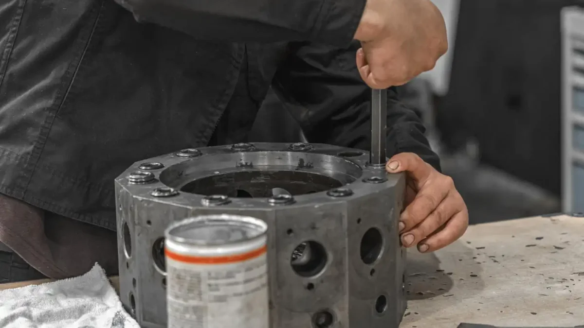 Trabalhador usando chave Allen para apertar parafuso em uma peça metálica grande sobre uma bancada.