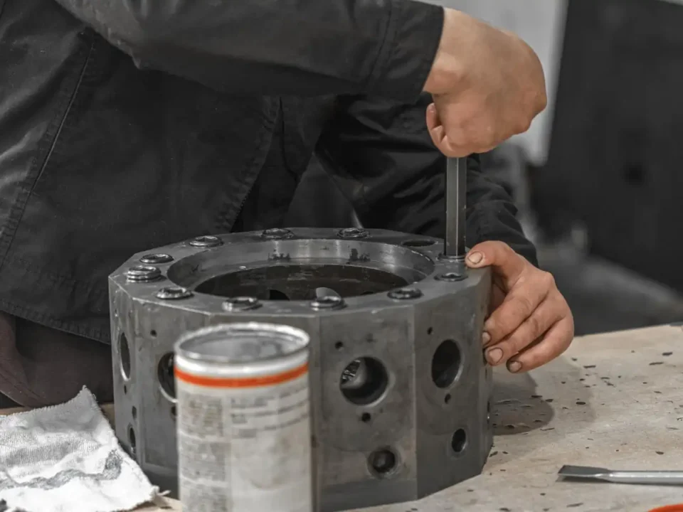 Trabalhador usando chave Allen para apertar parafuso em uma peça metálica grande sobre uma bancada.